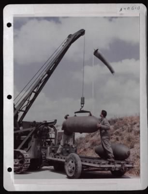 ␀ > Ornance Men Use Tractor Type Crane To Load 2000 Lb. Bombs Onto Special Truck-Type Dollies At A Base In England.