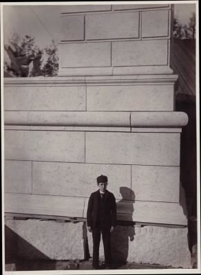 Thumbnail for Trustees' McKim Construction Photos > Boy poses in front of mock-up of cornerstone for McKim Building