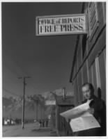 Thumbnail for Roy Takeno reading paper in front of office - photograph by Ansel Adams