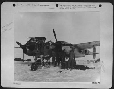 General > Ninth Air force mechanics work on this fighter at a snow-covered base somewhere in Belgium. Two men (right) get set to hook up pipes from heater to warm up the port engine.