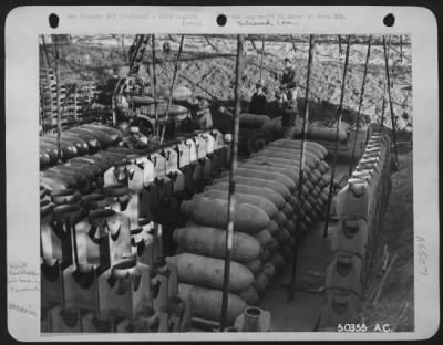 General > England-Ordnance crew under supervision of Capt. Harry Faulkner, Jersey City, N.J., loads 500 lb. high explosive bombs on to trailer with aid of crane. The revetment is covered by camouflage netting and rows of tail fins can be seen between