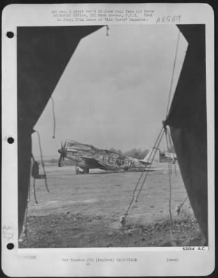 General > Camouflaged for the night is this North American P-51B, seen through a tent opening at a 9th Air force base in England. Naturally, an enemy pilot would rather destroy a Mustang on the ground than meet one in the air, for he knows the odds are against