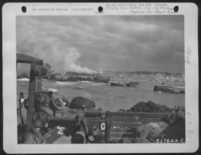 General > FRANCE-On the first day of the invasion, the 9th AF played a great supporting job in the landing with water proofed vehicles on this scene at the beachhead while 88 mm shells burst around them. In the background on the cliffs smoke soars