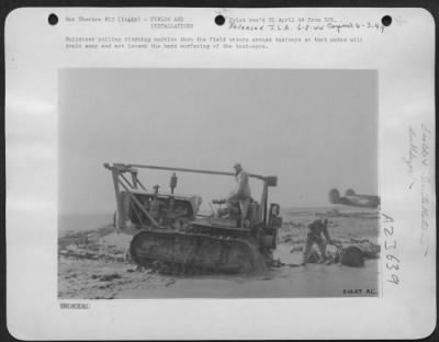 Consolidated > Bulldozer pulling ditching machine thru the field waters around taxiways so that water will drain away and not loosen the hard surfacing of the taxi-ways.