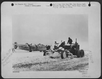 Thumbnail for Consolidated > Snow Forces A Halt In The Air War.  The Hooded Nose Of This Snow-Covered 15Th Aaf Consolidated B-24 Liberator Points Glumly To The Runway Blocked By Drifts And Mud.  A Grader, Manned By An Aviation Engineer, Is Clearing A Path At This Italian Base So That