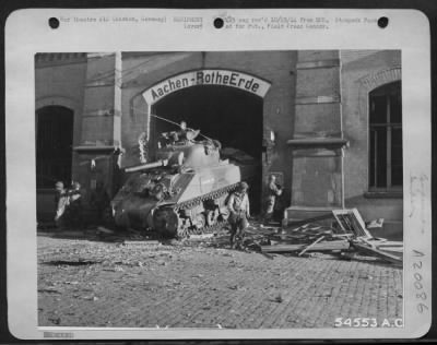 Consolidated > The first U.S. tank to enter Aachen, Germany, rumbles through a hole opened in the railroad station by a tank-dozer. As the tanks, tank-destroyers and other heavy armament awaited the termination of a bombardment by 9th AF dive-bombers before