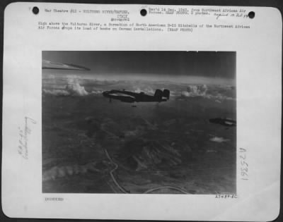 Consolidated > High above the Vulturno River, a formation of North American B-25 Mitchells of the Northwest African Air Forces drops its load of bombs on German installations.