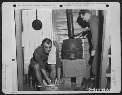 General > Lt. Wayne E. Comment of Fort Wayne, Indiana takes a "sectional" bath while his buddy, Lt. Robert J. Todd of Tampa, Florida, stokes up the stove in one corner of their "Shackteau," a two-story tent which they constructed at a 9th Air Force base