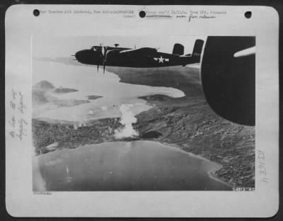 Consolidated > North American B-25 Mitchell bombers of the 13th AAF are pictured here winging their way over the Rataval supply area, New Britain, after having dropped their bombs on this target for the day. A large fire can be seen on the shore of Talili Bay