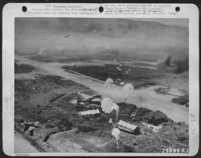 Consolidated > Parachute bombs are dropping from low-flying U.S. planes on revetments protecting dispersed Jap craft on the runway and on tents, huts, and a truck at Vunakanau Airfield, Rabaul, New Britain. Note plane nosed in ditch at lower left, and other planes