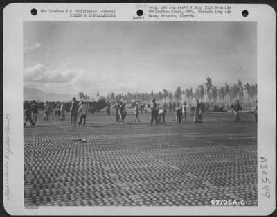 Consolidated > Hundreds of Filipinos help American soldiers bolt the steel mat into place during construction of a landing strip in the Philippine Islands.