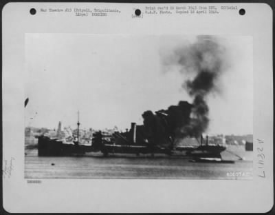 Thumbnail for Consolidated > A seven thousand ton ship, anchored at Tripoli, Tripolitania, was hit directly by two 250 pound bombs during an attack by eight Blenheims on enemy shipping. One of the planes crashed into a torpedo boat (background) which burns furiously. 9 July