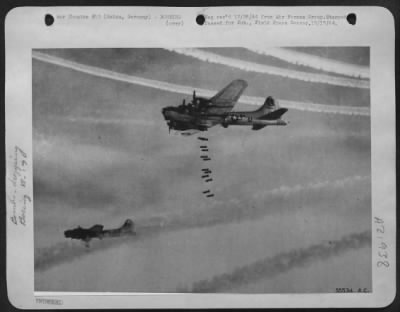 Consolidated > Boeing B-17 Flying Fortresses of the 8th Air Force send their bombs plummeting through clouds on to the important railway marshalling yards at Mainz, Germany. Eerie white vapor trails make a split rainbow over the target as the first of the bombers