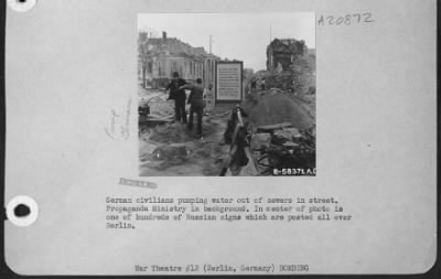 Consolidated > German Civilians Pumping Water Out Of Sewers In Street.  Propaganda Ministry In Background.  In Center Of Photo Is One Of Hundreds Of Russian Signs Which Are Posted All Over Berlin.