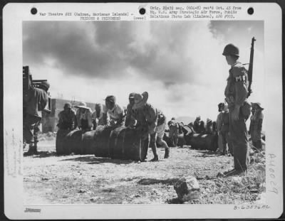 Consolidated > Japanese Soliders And Civilian Prisoners Of War Rolling And Stacking Gasoline Drums At A Supply Dump While Pvt. William E. Regan Of 170-01 91St Road, Woodhaven, Long Island, New York, Stands Guard.  Saipan, Marianas Islands, 29 June 1944.